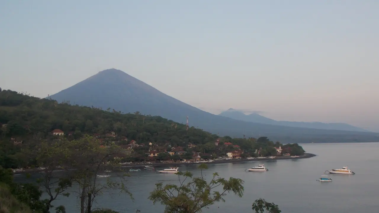 Fishing boats at anchor in the bay at Amed, with the cone of Mount Agung rising beyond the shore.