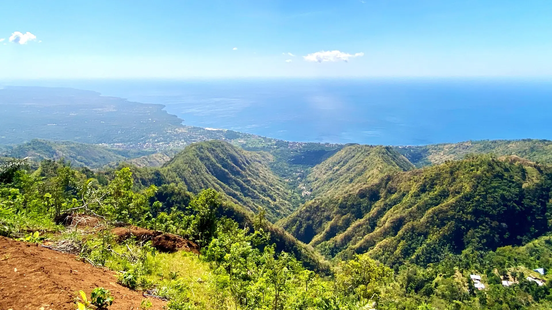 Green ridges and valleys of the Karangasem coast falling away to a blue sea.