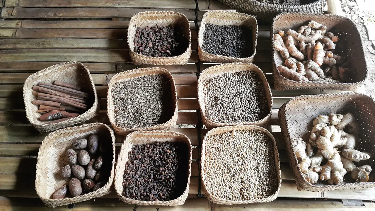 Woven baskets of whole spices laid out in rows, among them cinnamon, black pepper, turmeric and ginger.